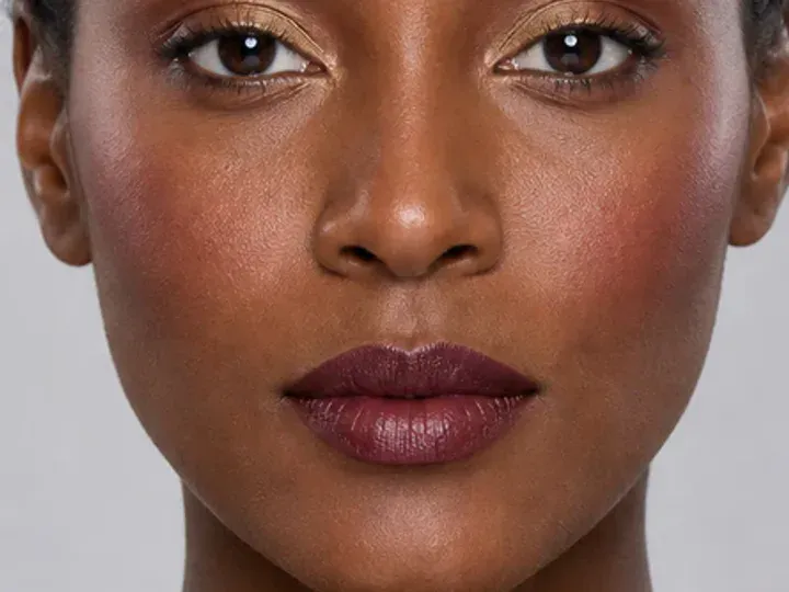 Step 2 of Rich Berry and Gold Makeup for Deep Skin, showing discoloration is softened while natural skin remains visible around the perimeter of the face.